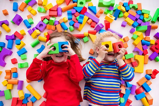 Happy preschool age children play with colorful plastic toy blocks. Creative kindergarten kids build a block tower. Educational toys for toddler or baby. Top view from above.